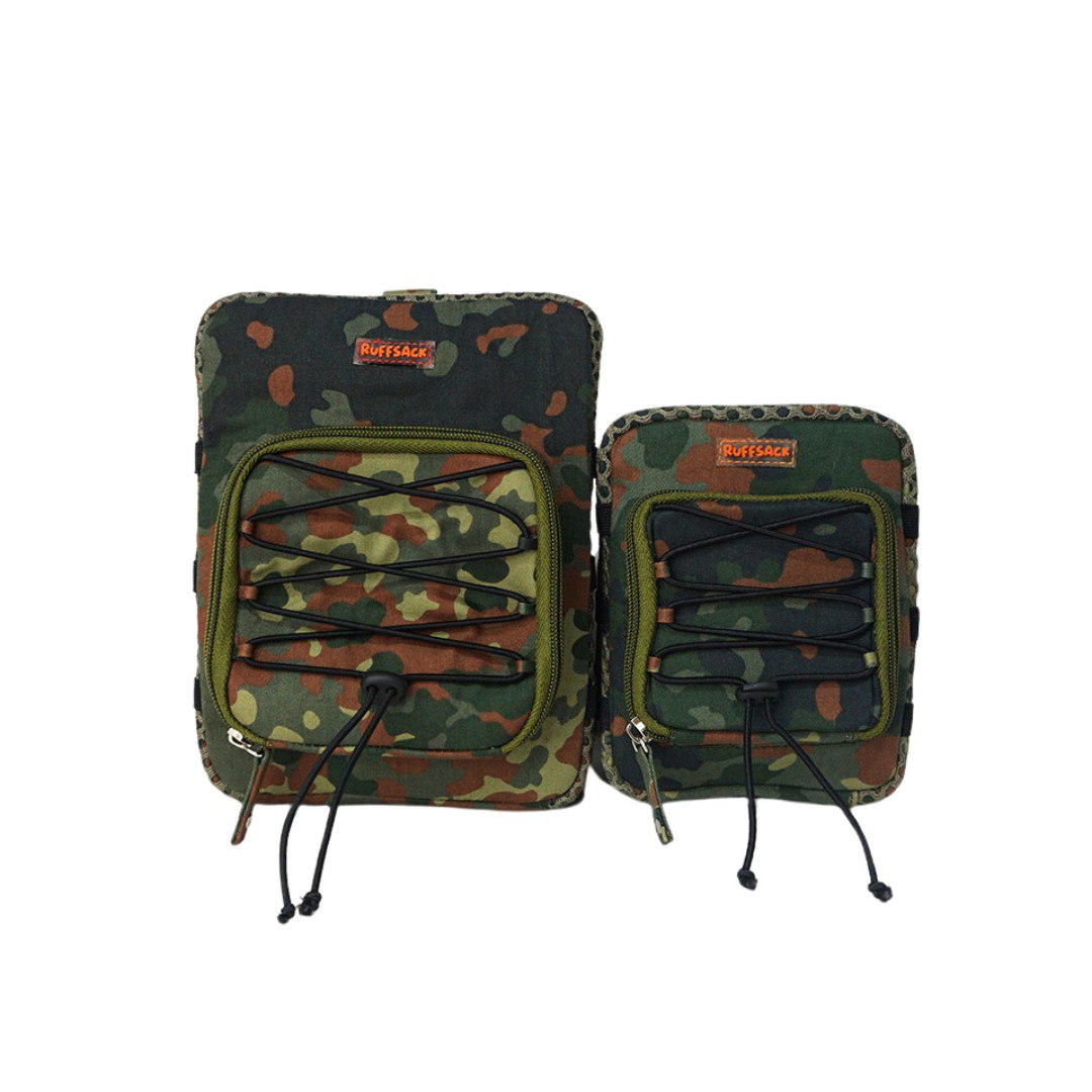 Scout model Ruffsack backpack front angle. The backpack features a camouflage cotton fabric with a net style fabric with elastic straps along the sides and front. A front zipper allows access to the inside.