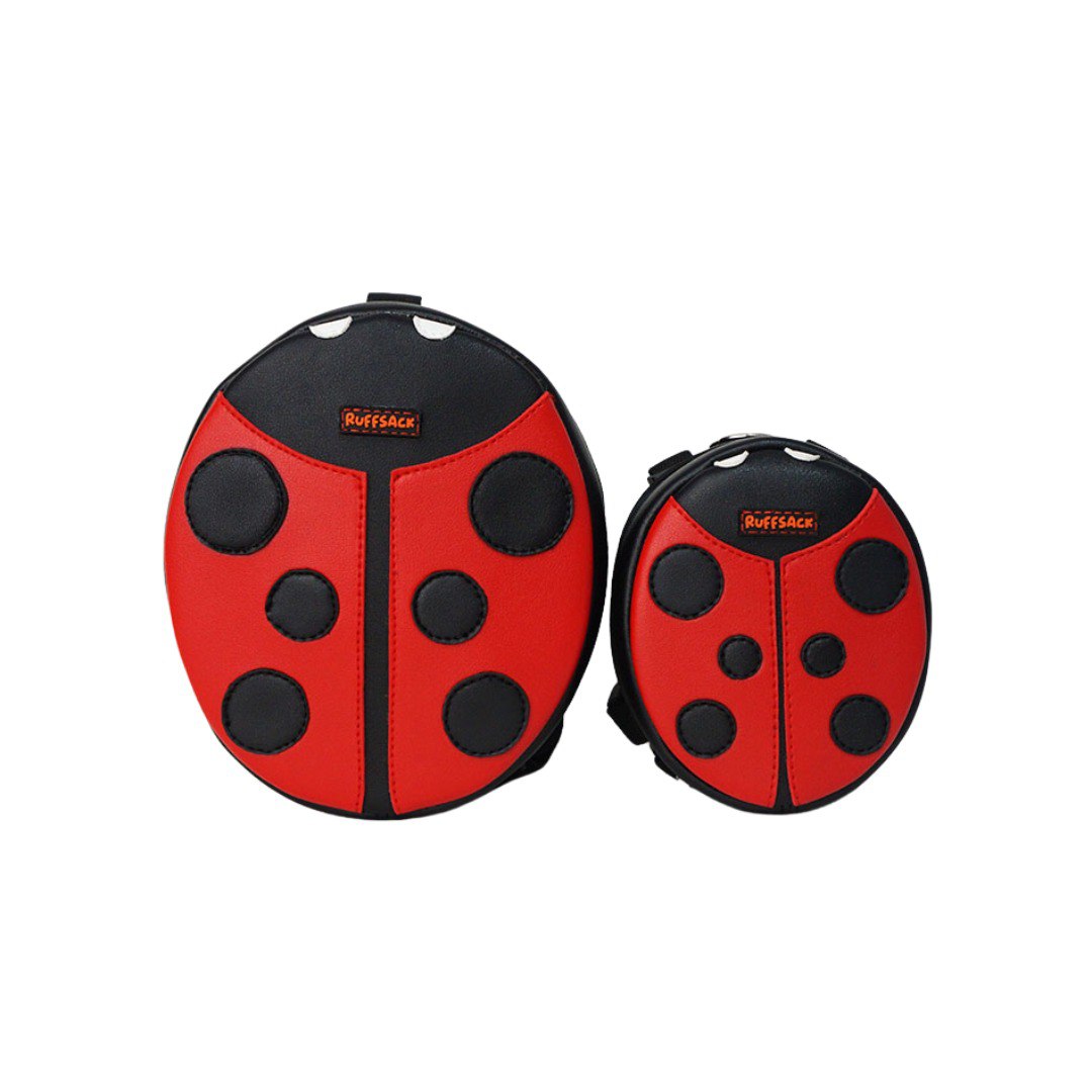 Lucy Ladybug model Ruffsack backpack front angle. The backpack features an oval ladybug shape made with faux leather red wings, black spots, black head, and white eyes. A side zipper allows access to the inside. Straps are black in color.