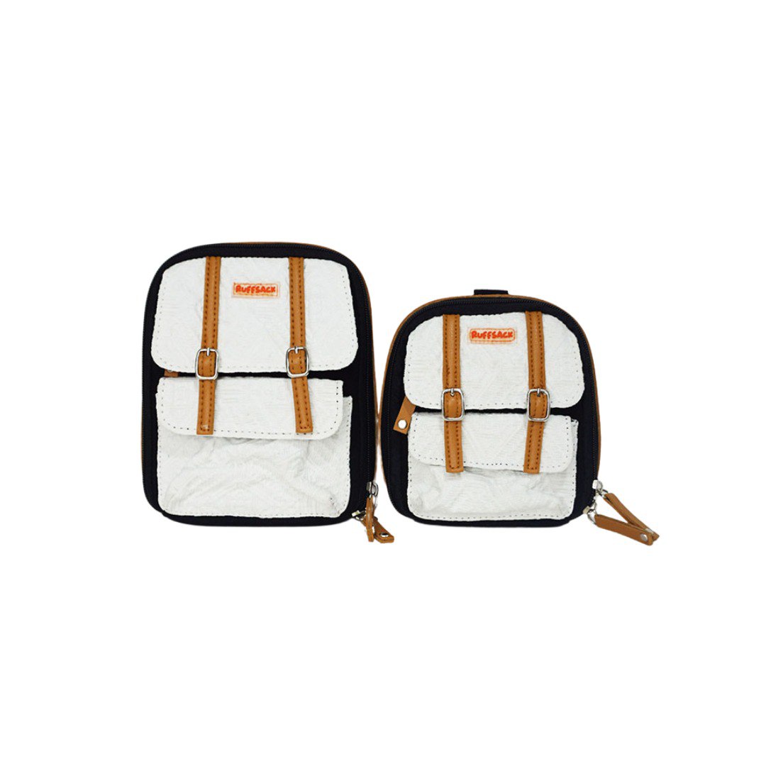 Dale Black and White model Ruffsack backpack front angle. The backpack face features a cotton white embossed pattern with two small front buttoned pockets atop a cotton black solid pattern. Tan faux leather accents are on the front and sides of the bag. A side zipper allows access to the inside.
